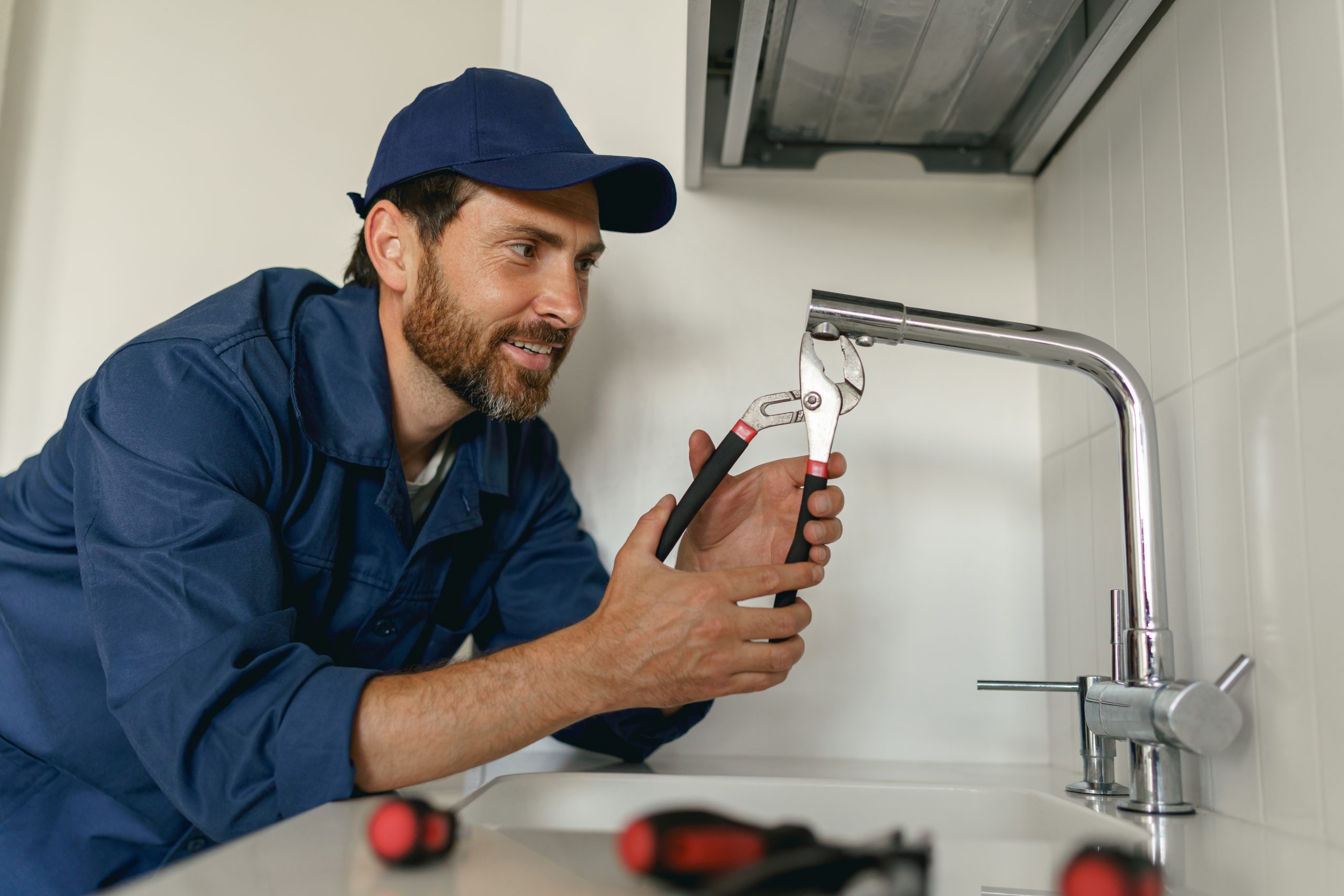 Professional plumber in blue uniform fixing broken water tap in kitchen. Repair service concept